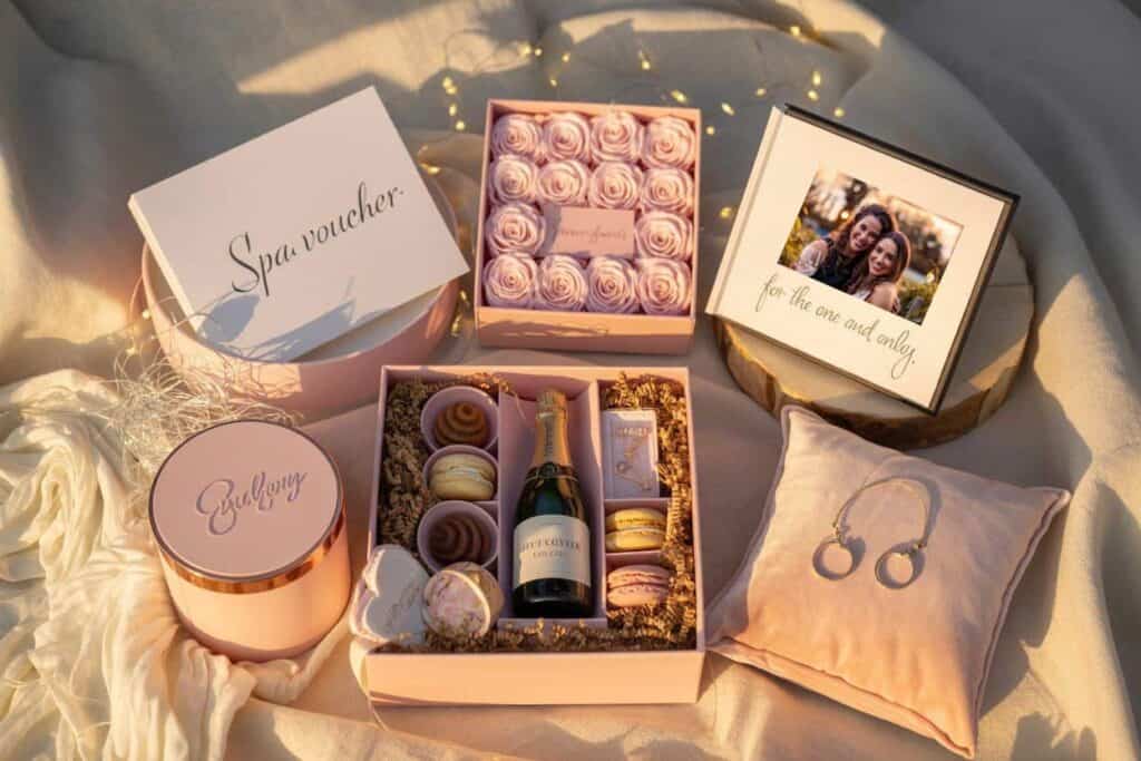 Ideas de regalos de cumpleaños para amigas con vale de spa, rosas, álbum de fotos, joyería y una caja de regalo con dulces y champán.
